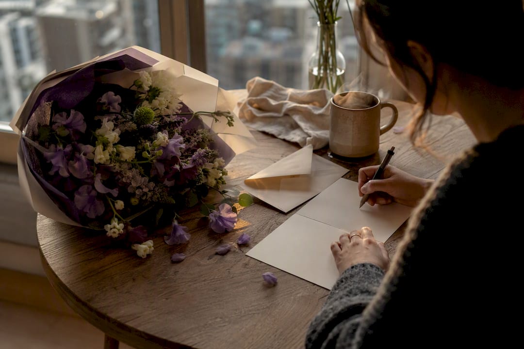 Hand writing anniversary card next to fresh flowers