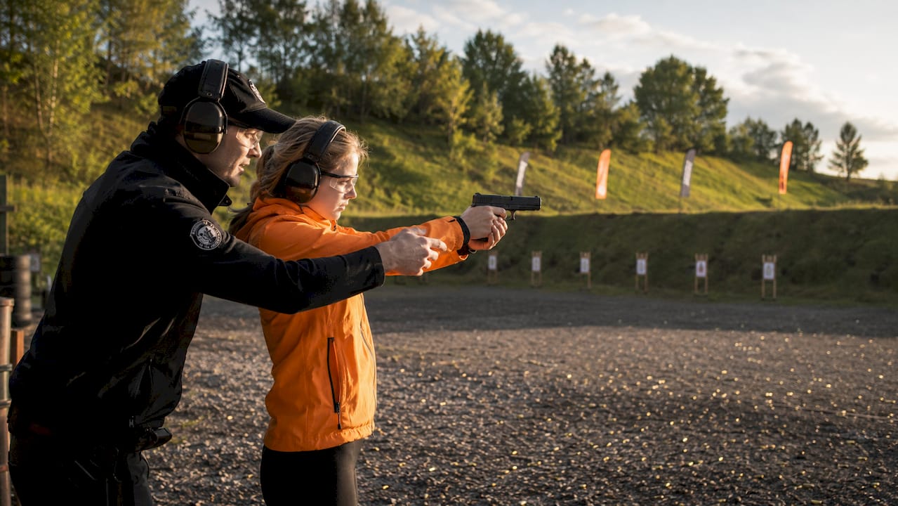 Instructor guiding beginner pistol shooter indoors