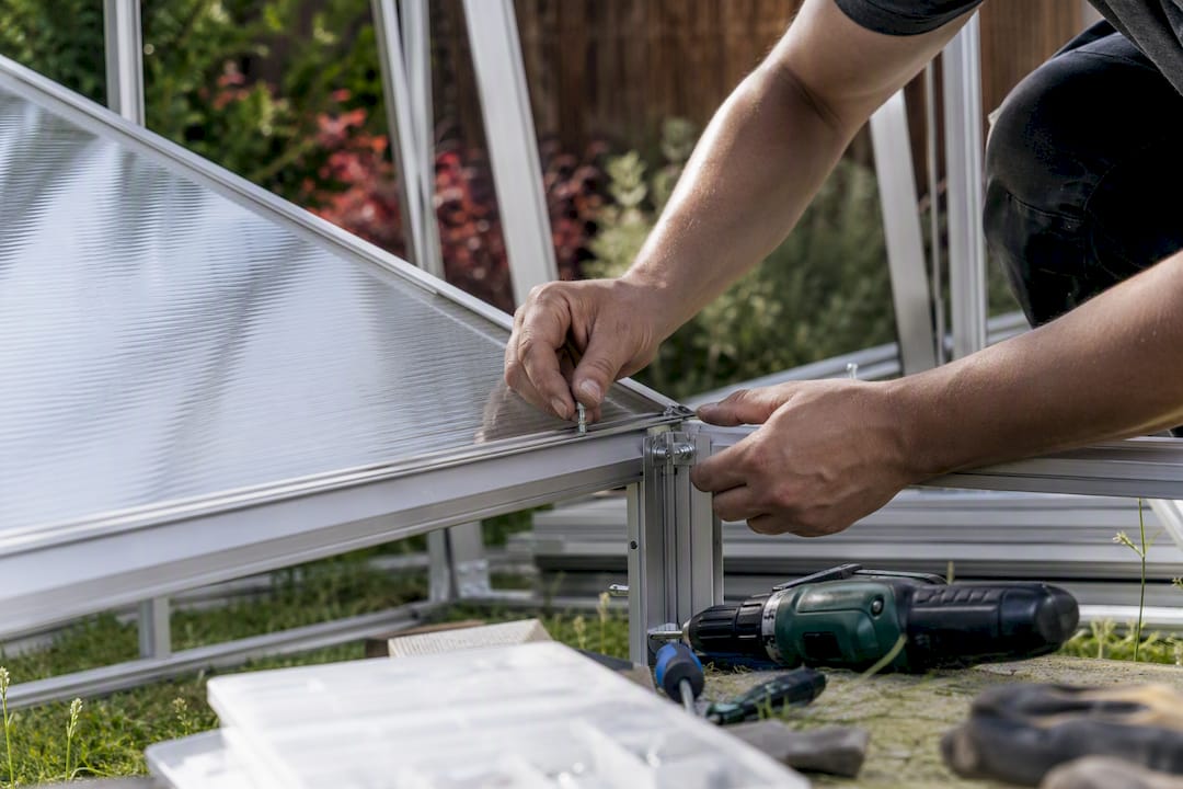 Hands installing polycarbonate glazing on greenhouse frame