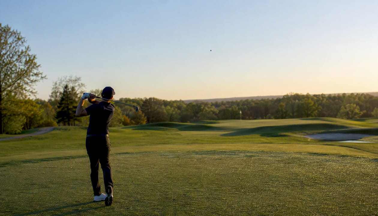 Golf ball curving in flight over green fairway