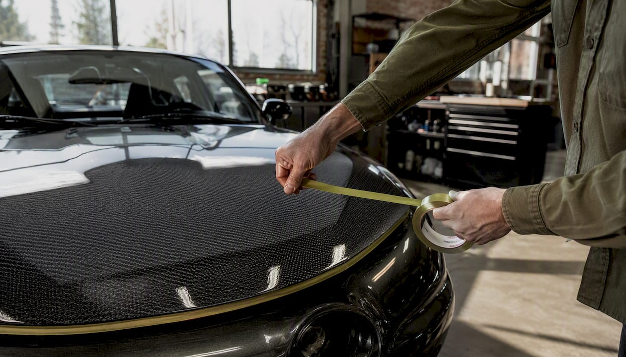 Hands applying painter’s tape to carbon fiber hood edge