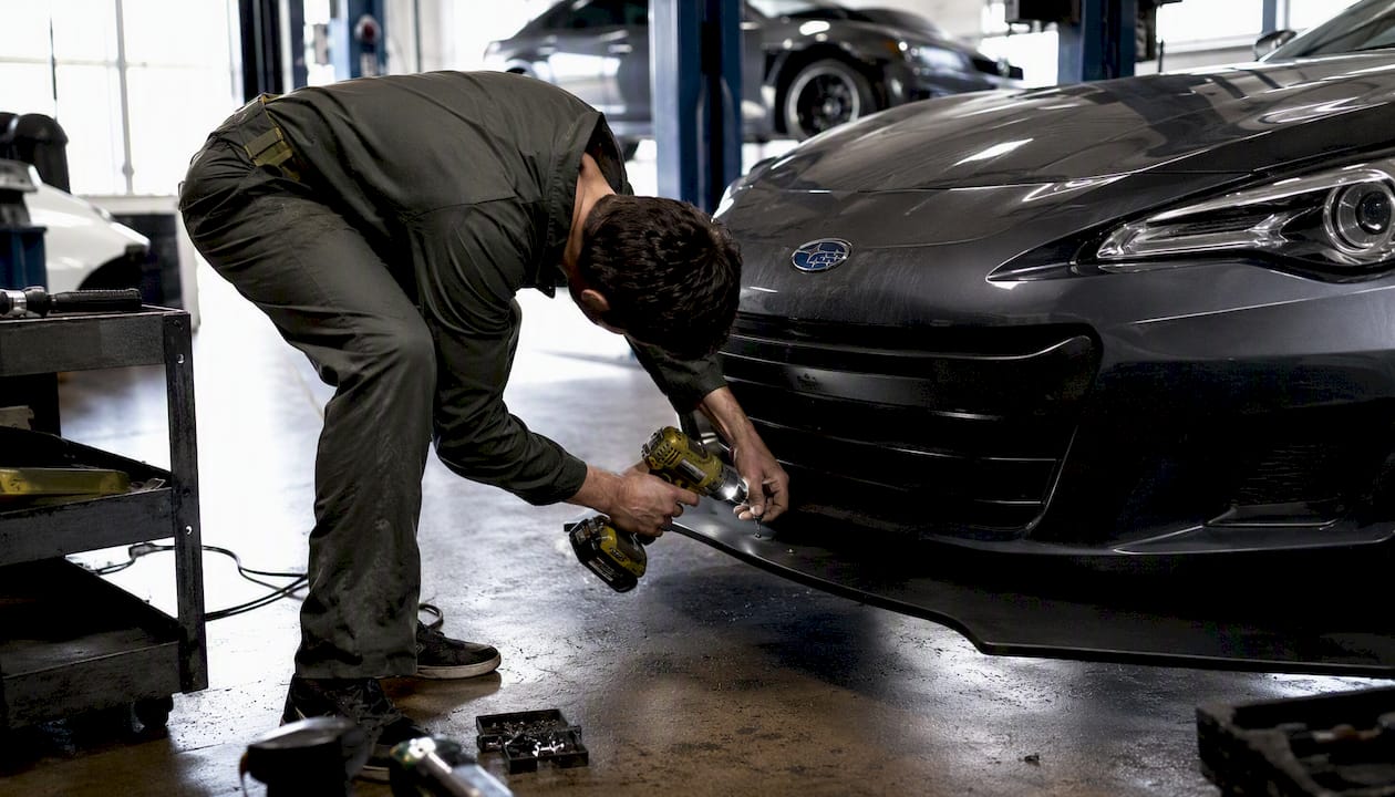 Technician installing front lip on Subaru BRZ in garage