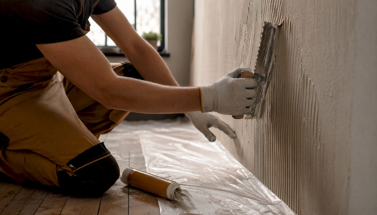 Hands applying adhesive to wall surface