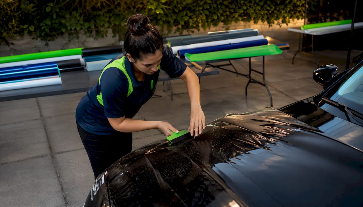 Woman applying vinyl wrap to car hood indoors