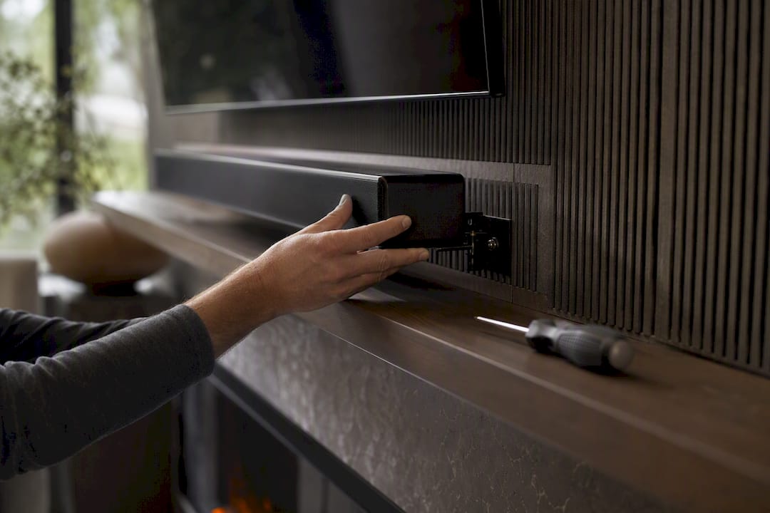 Hands installing soundbar below fireplace media wall