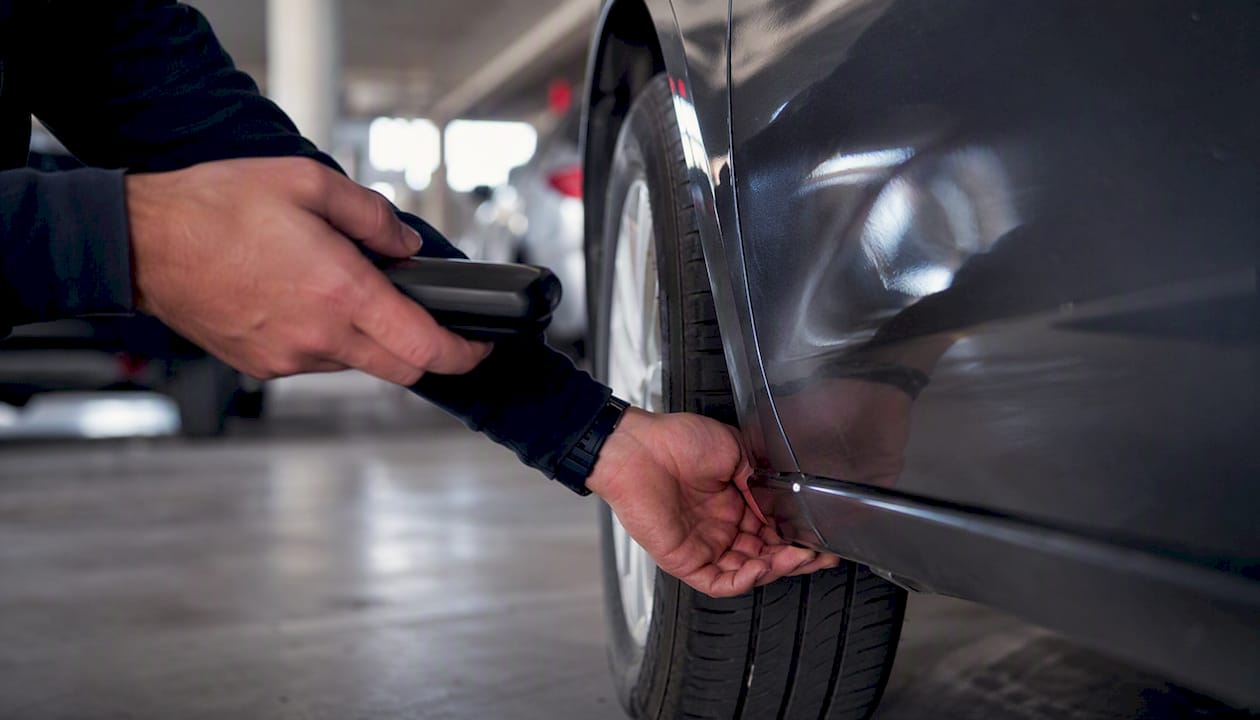 Hands inspecting car side panel and tire tread
