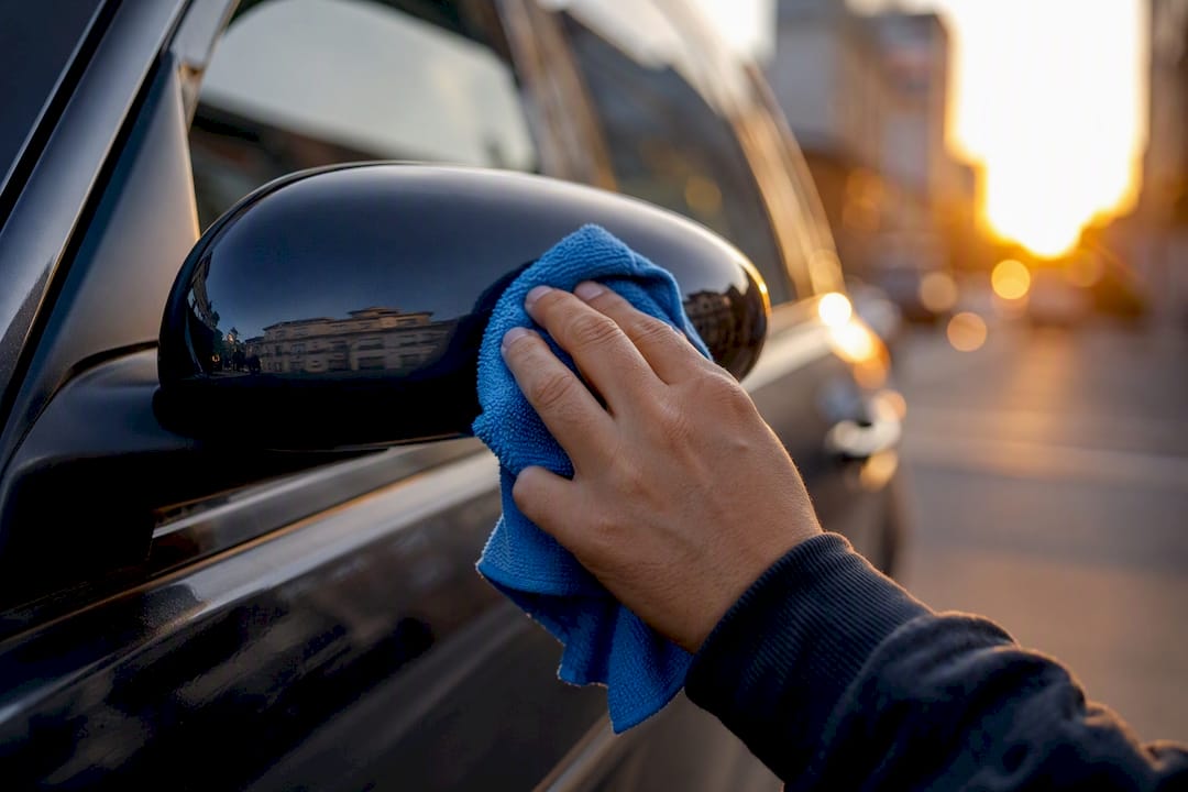 Hand cleaning car mirror in driveway