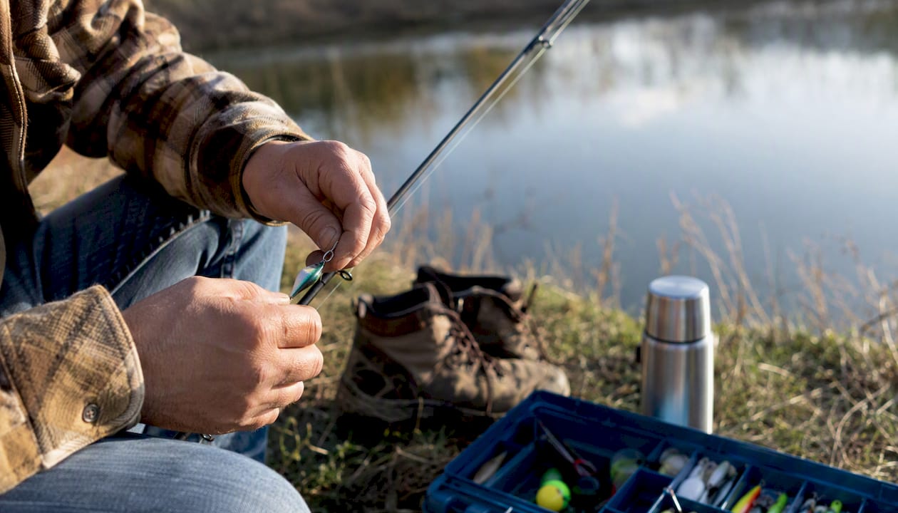 Hands preparing fishing gear by a lake