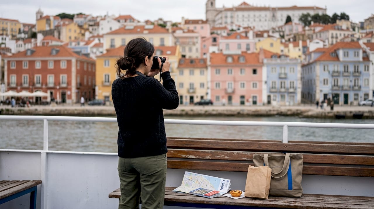 Tourist photographing Alfama from boat deck