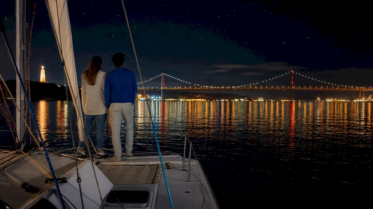 Two friends on catamaran viewing Lisbon night skyline