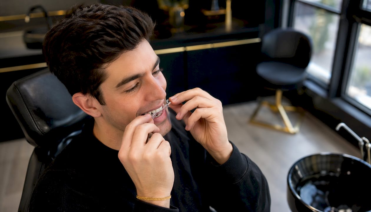 Hands placing dental whitening tray on teeth