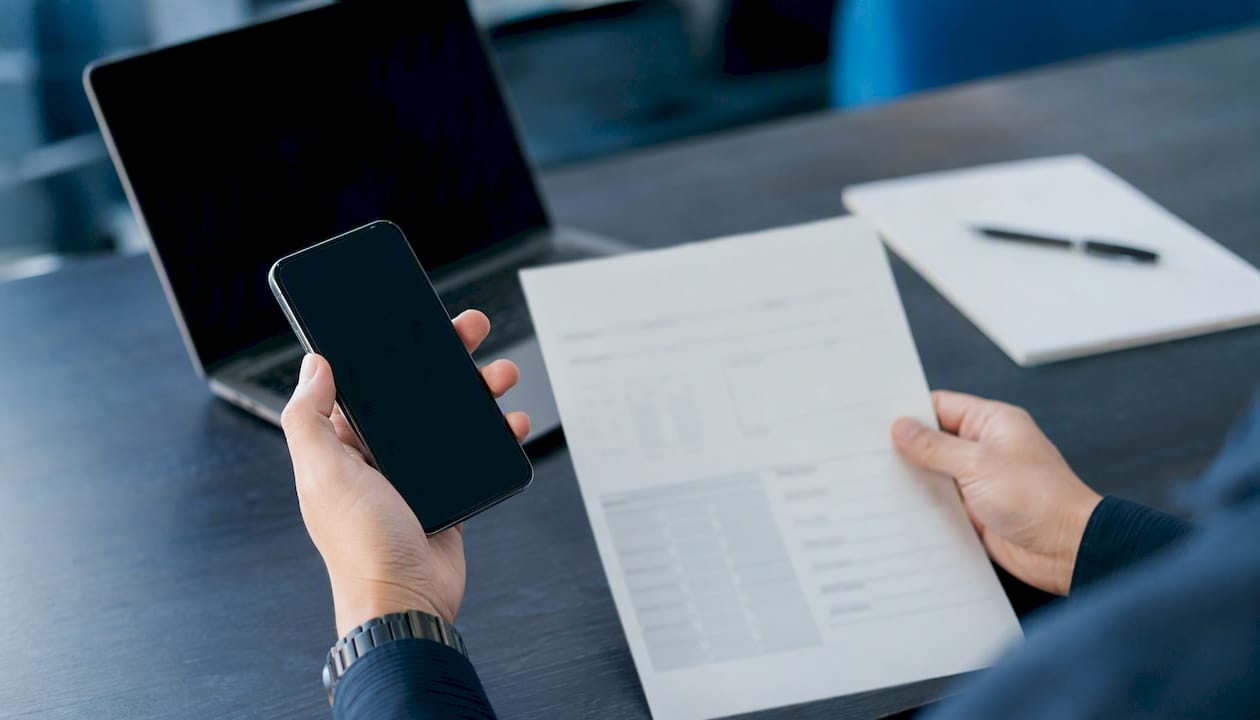 Hands holding smartphone and a printed chart on desk