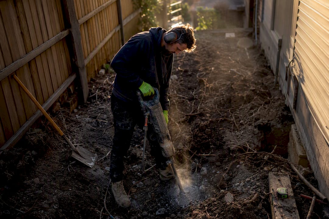 Worker jackhammering soil at home foundation