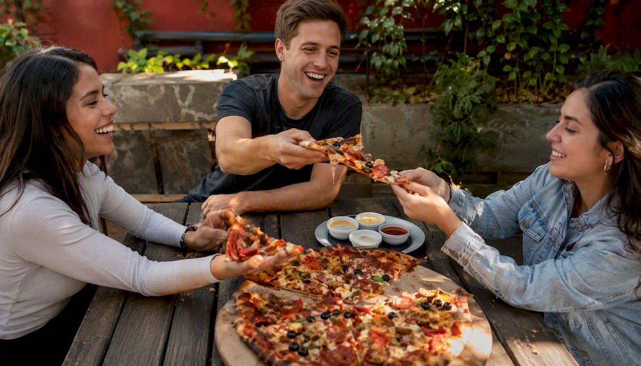 Hands dividing pizza and shared appetizers