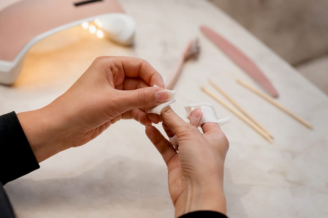 Handen die watjes met aceton om de nagels wikkelen om gellak te verwijderen.