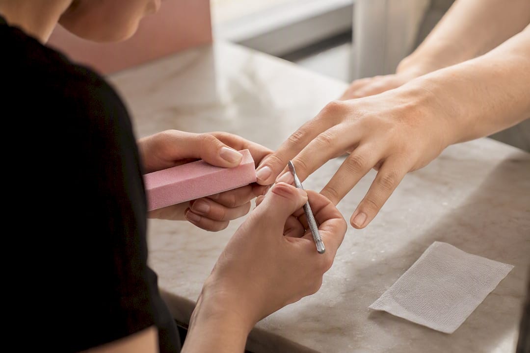 Handen die nagels verzorgen met een polijstvijl en een cuticle duwer