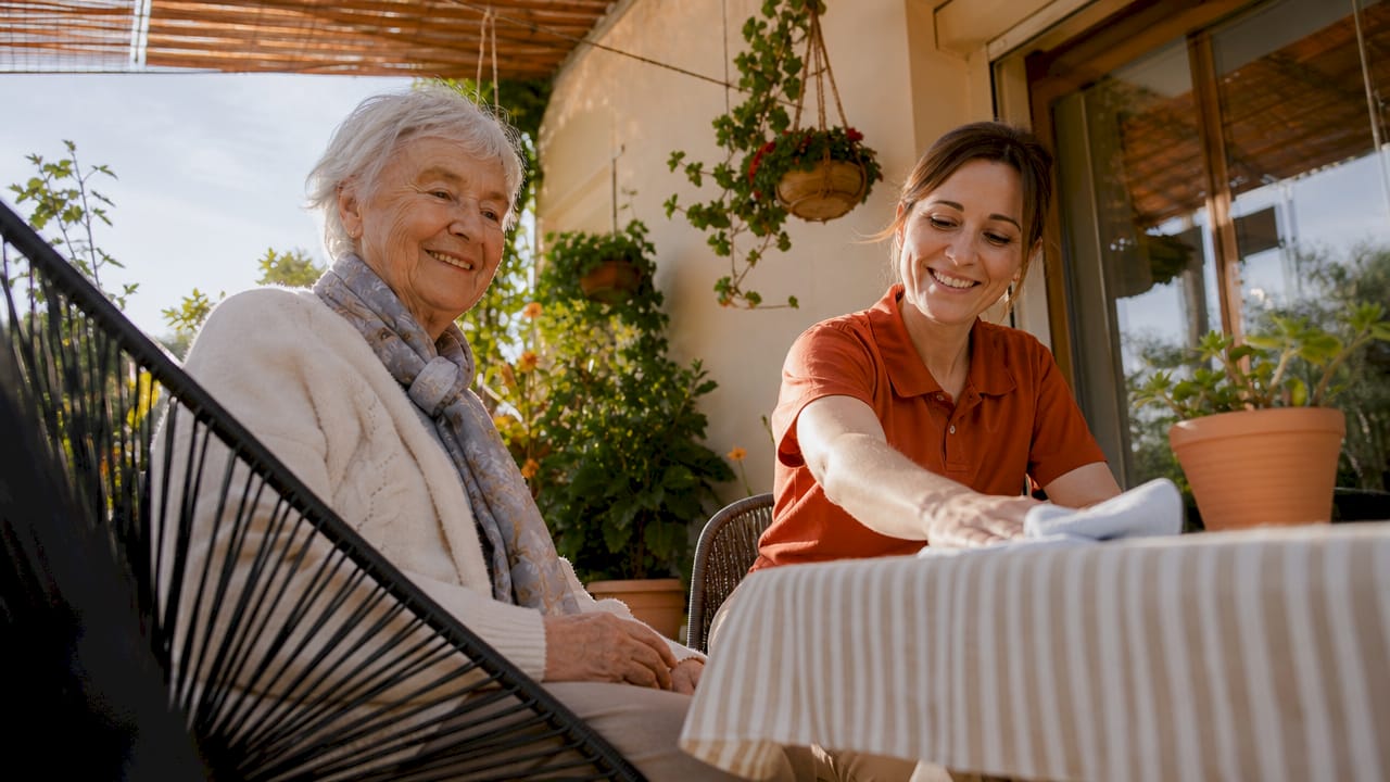 Eine Betreuungskraft begleitet eine ältere Frau auf der Terrasse ihres Hauses.