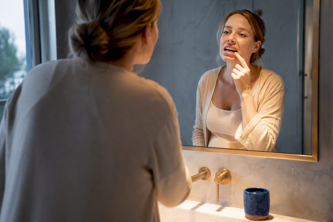 Pregnant woman checking gum sensitivity in mirror