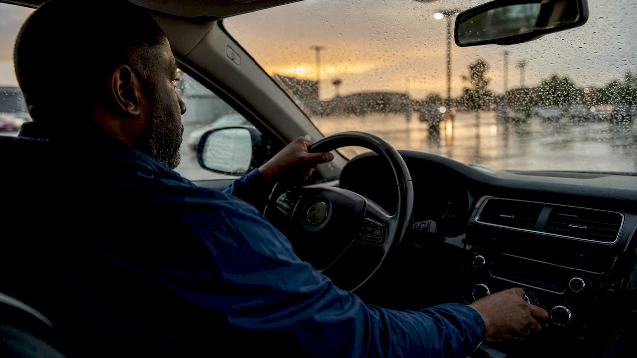 Una mano regula los mandos del coche mientras la lluvia golpea el parabrisas.