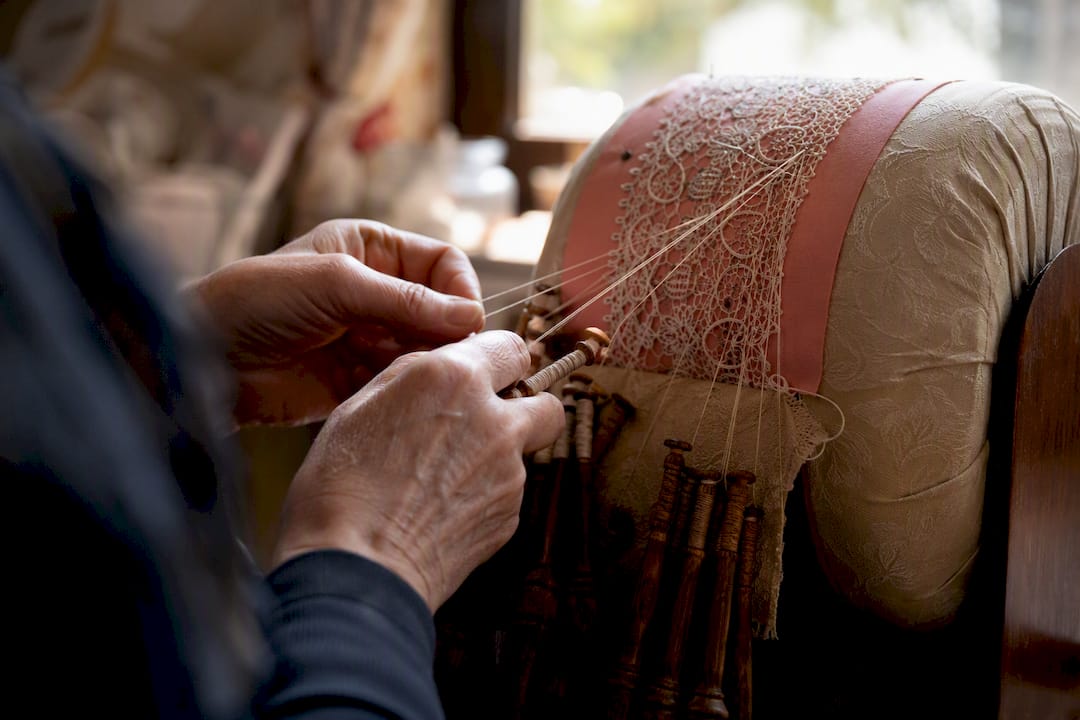 Hands crafting handmade lace with bobbins