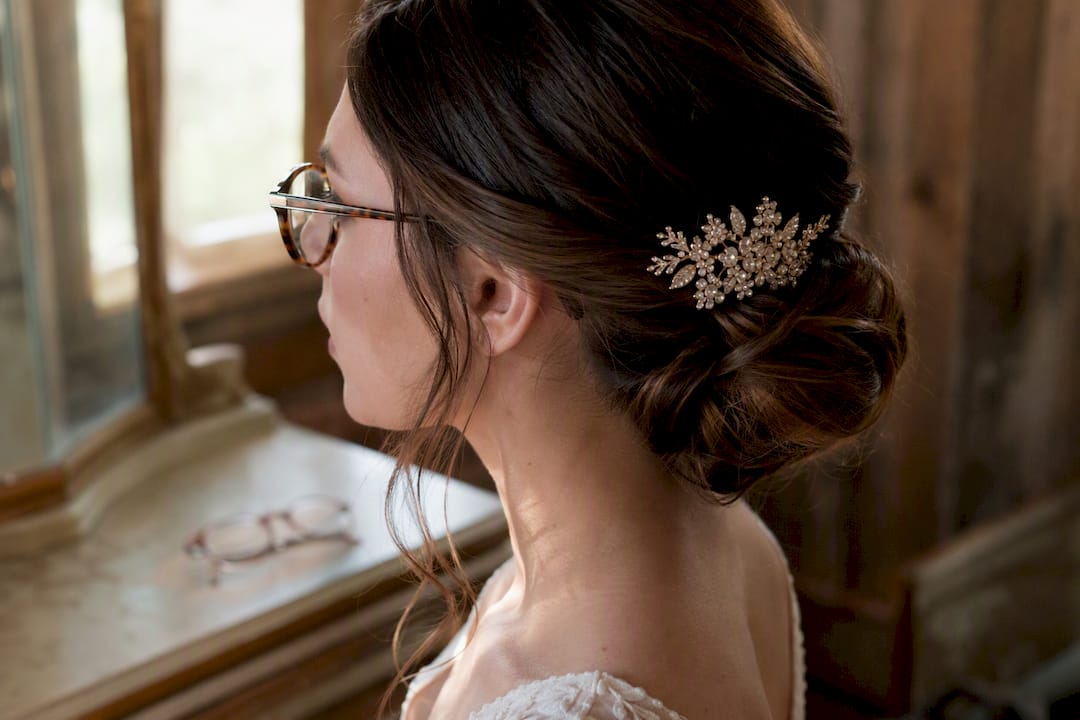 Low bun hairstyle with bridal hair comb and glasses nearby
