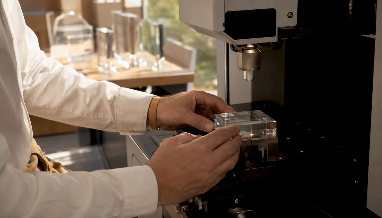 A 3D laser engraving on glass is performed with skillful hands.