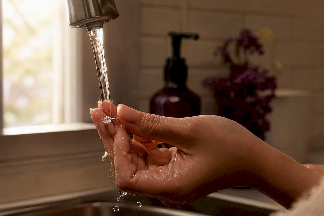 Hand rinsing moissanite ring under faucet water