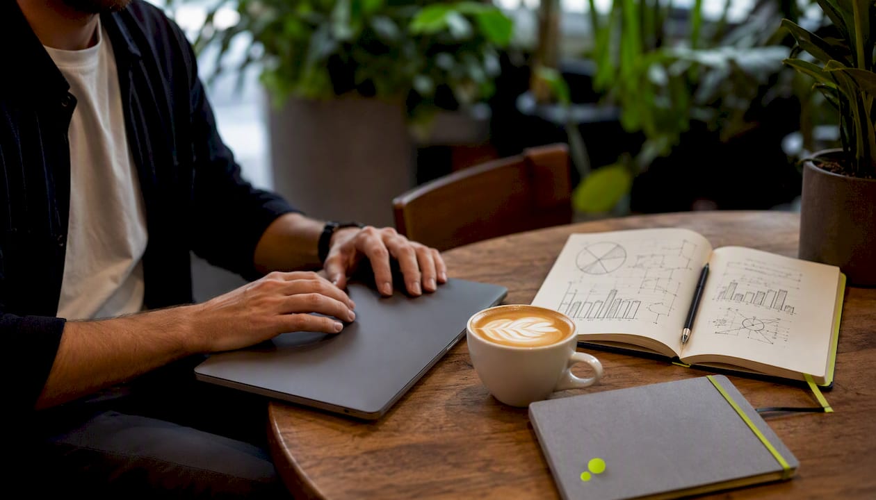 Van bovenaf gefotografeerde handen bij een laptop en een kop koffie