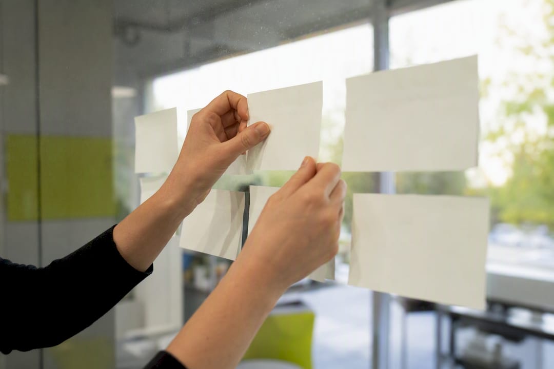 Handen die blanco plakbriefjes op een glazen bord ordenen