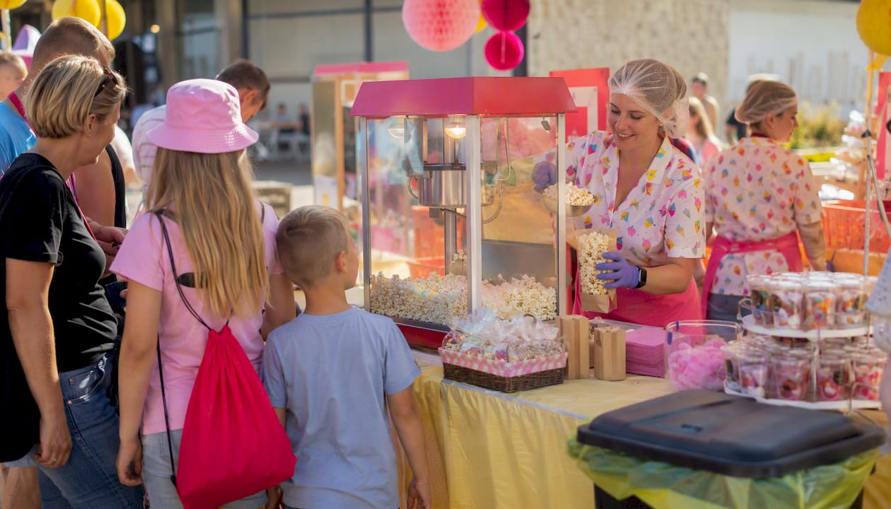 Vid festivalområdet står en popcornvagn där personalen snabbt fyller på de färgglada burkarna medan besökarna köar för att få nypoppade popcorn.