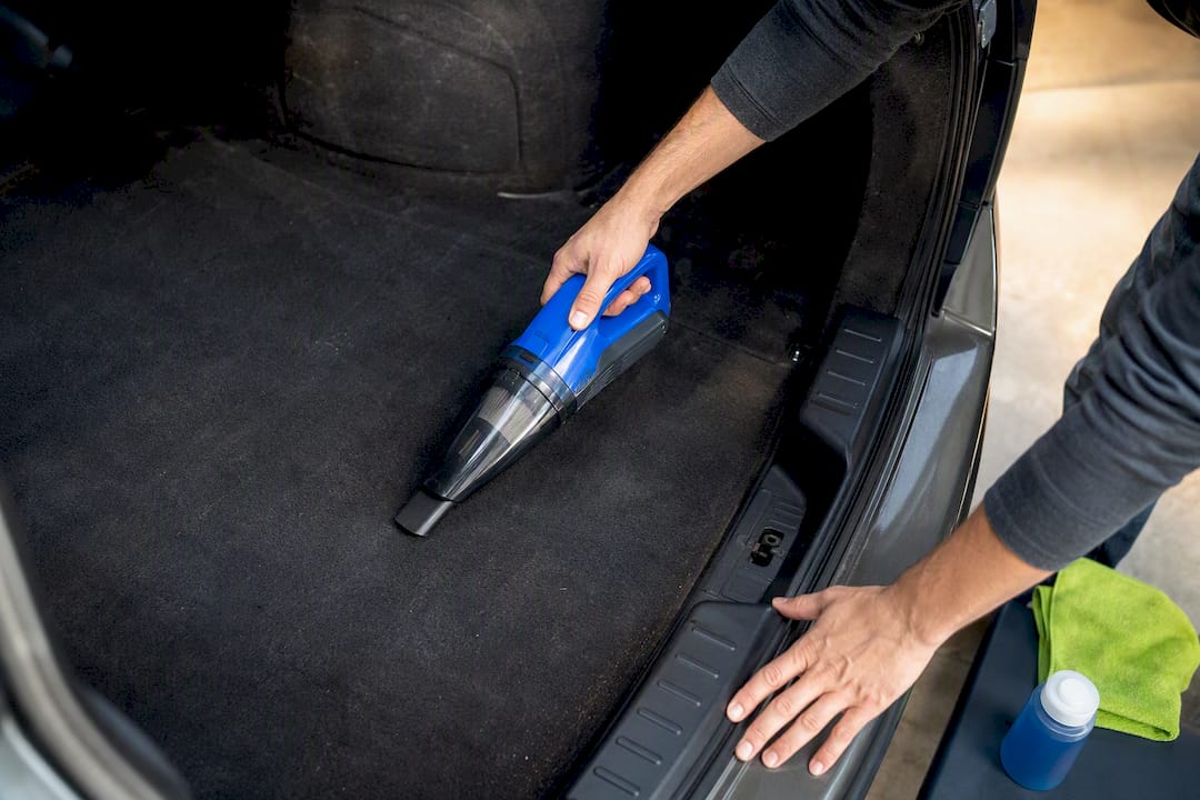 Hands vacuuming an older car trunk