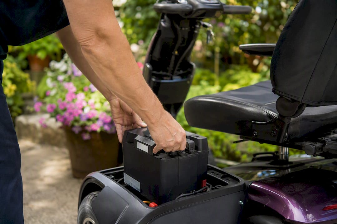 Hands handling mobility scooter battery outdoors
