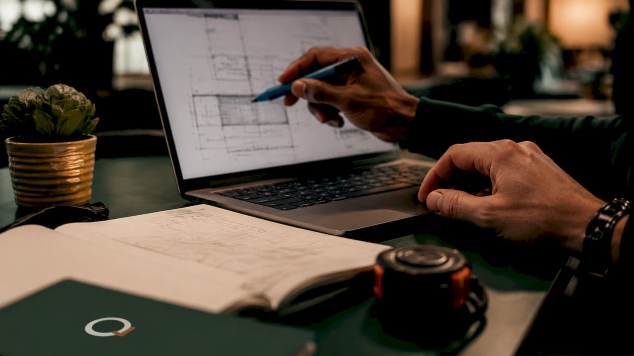 Hands cross-referencing PDF construction details on laptop