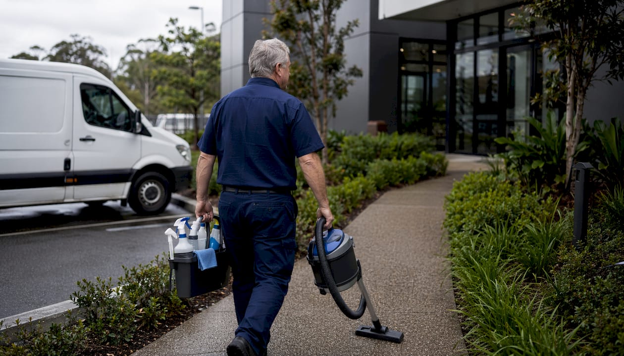 Cleaner walking with supplies near commercial building