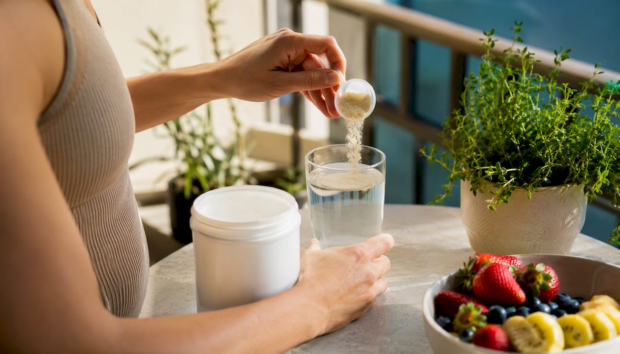 Hands pouring collagen powder into glass