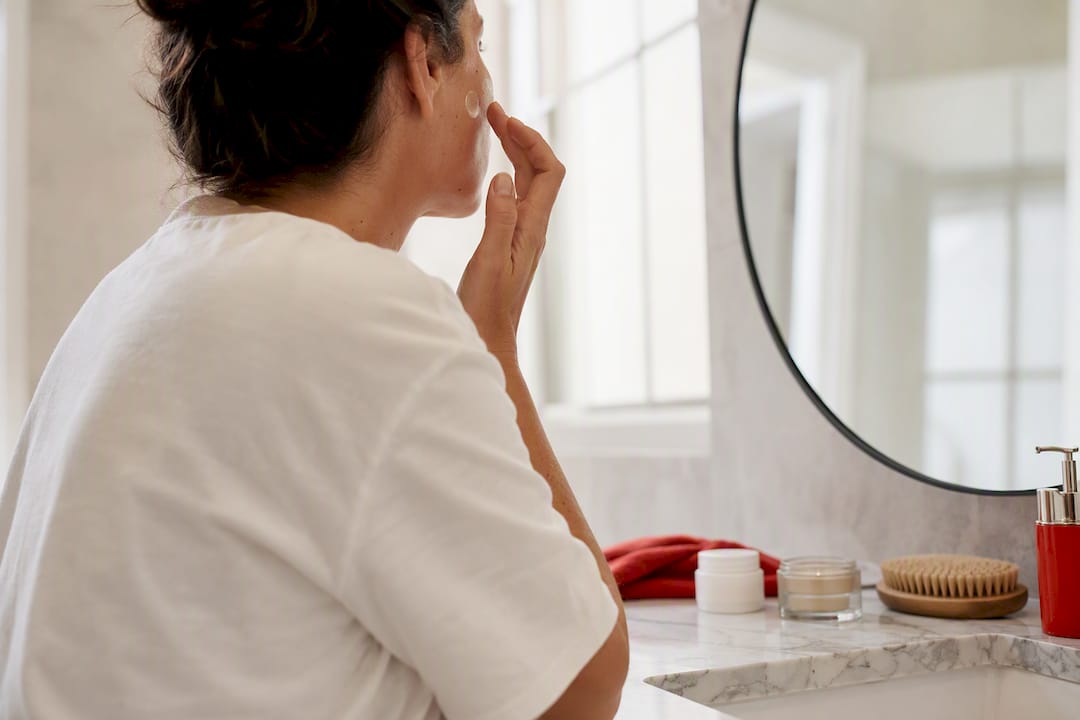 Woman applying retinoid cream at bathroom sink