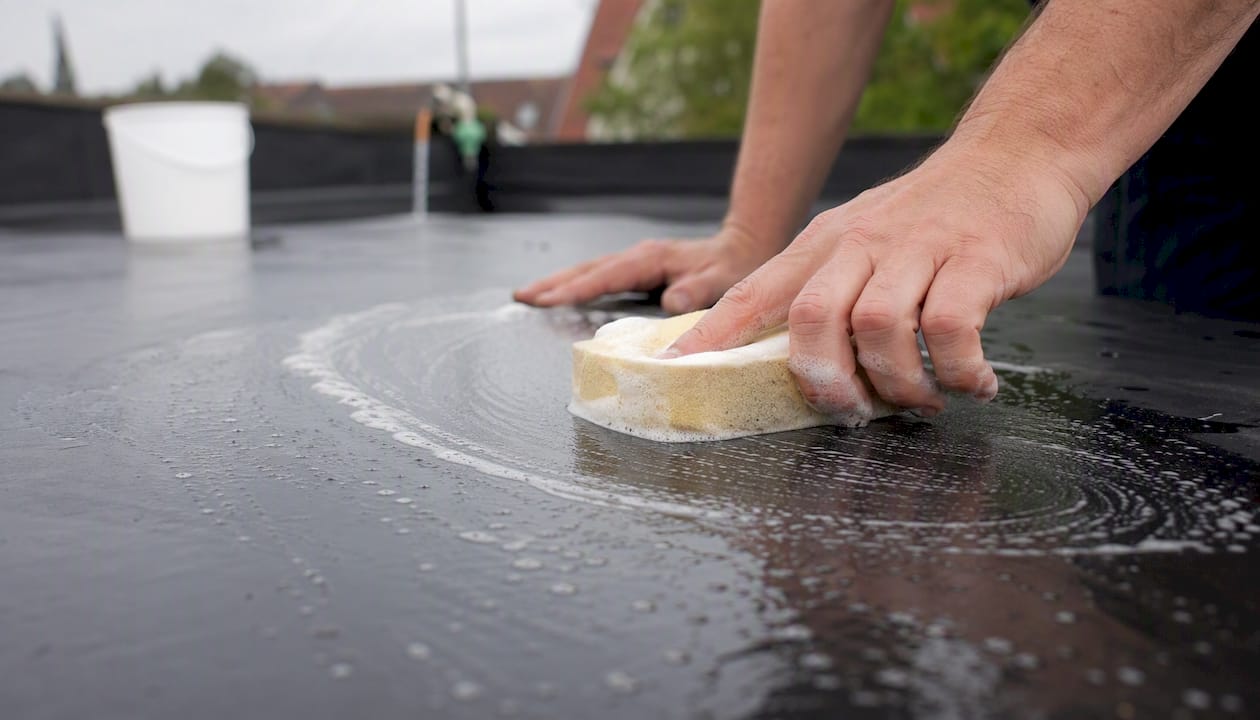 Met een spons en wat sop worden de handen gebruikt om het EPDM dak grondig schoon te maken.