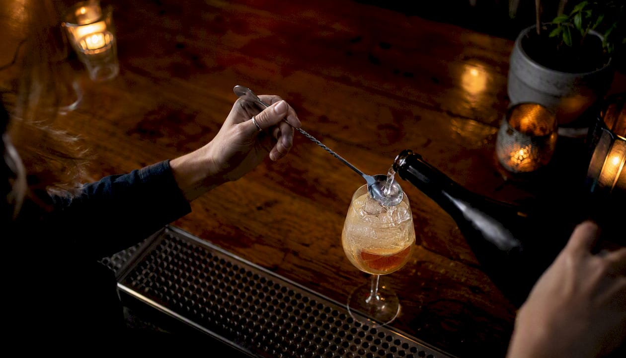 Pouring prosecco over inverted bar spoon into cocktail
