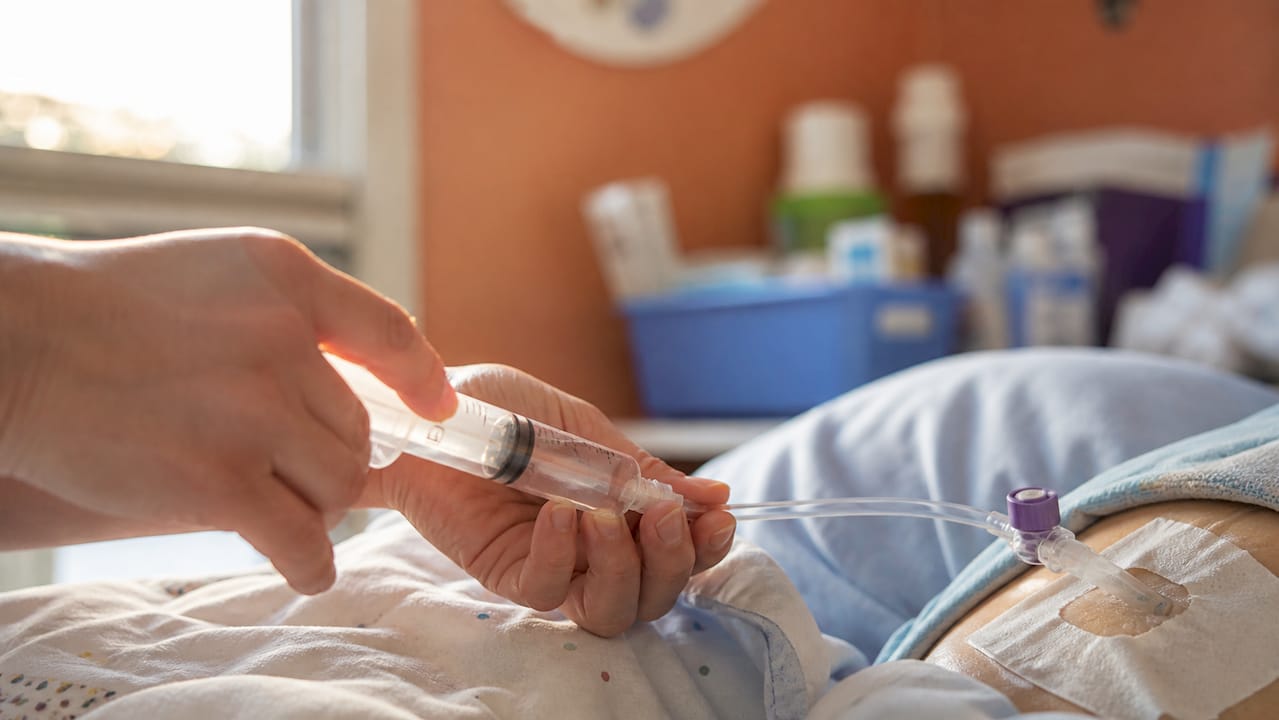 Hands flushing g-tube with warm water syringe