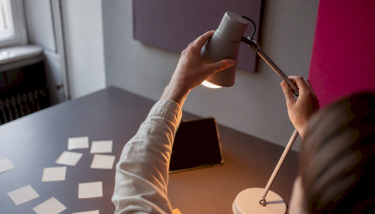 Hands adjusting desk lamp near digital device