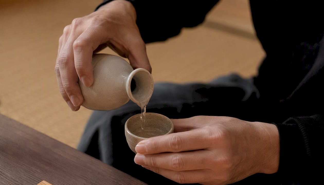 Hender som serverer sake i tradisjonelle japanske små kopper og flaske.