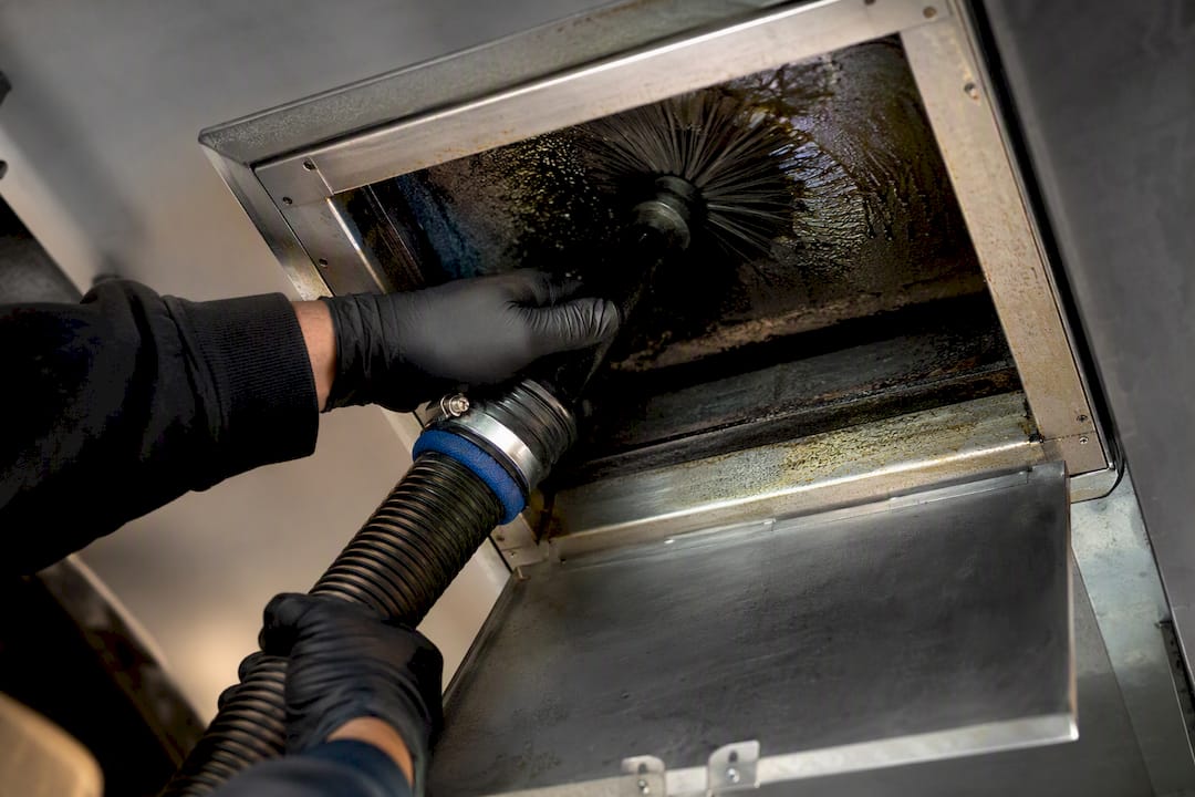 Technician cleaning grease from exhaust duct interior