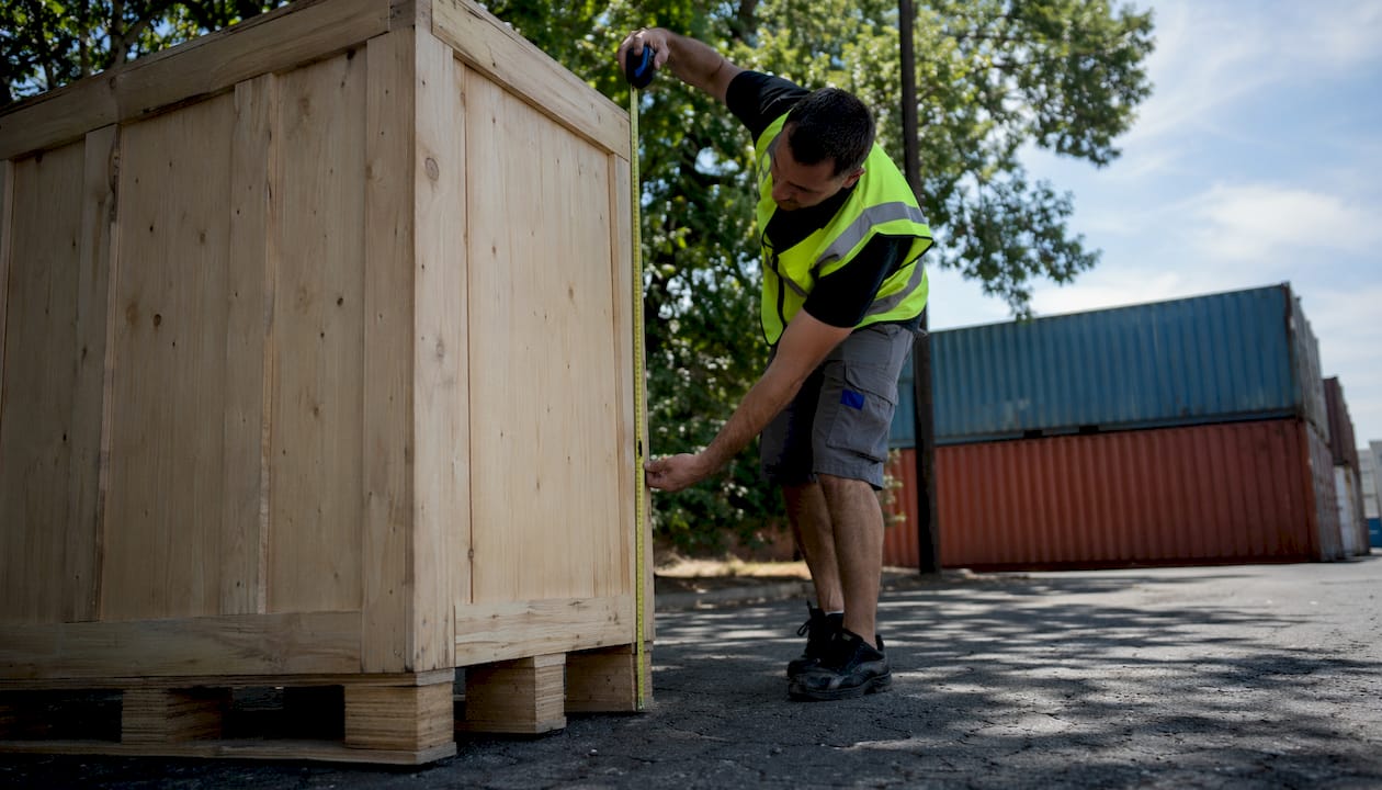 Worker measuring large freight crate in warehouse