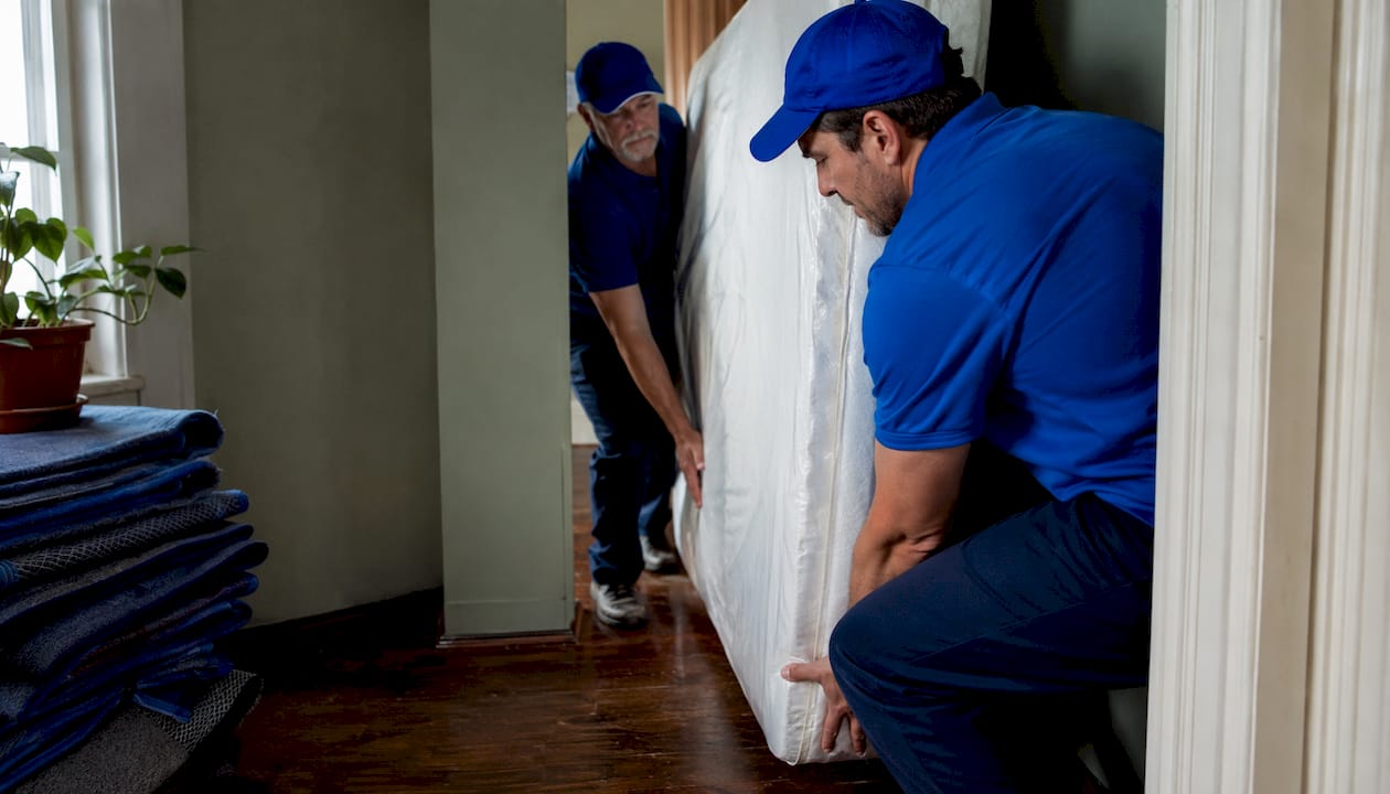 Two movers carrying mattress in apartment hallway