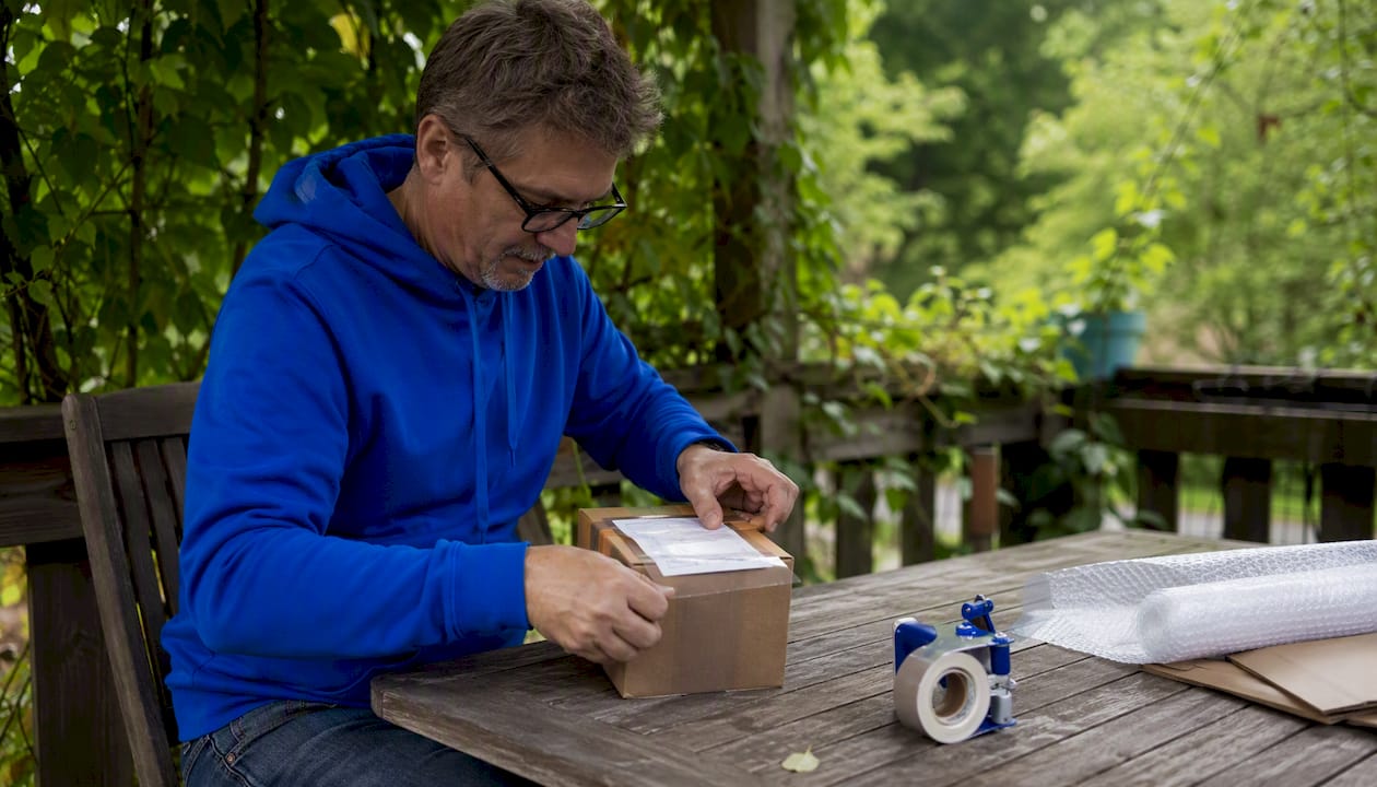 Seller taping package with shipping label in kitchen