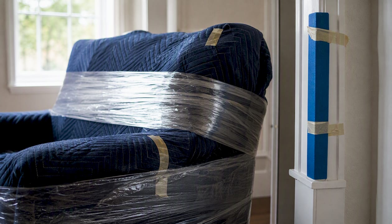 Couch wrapped with moving blankets near protected doorway