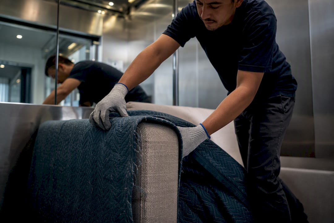 Mover wrapping sofa armrest with protective blanket in elevator