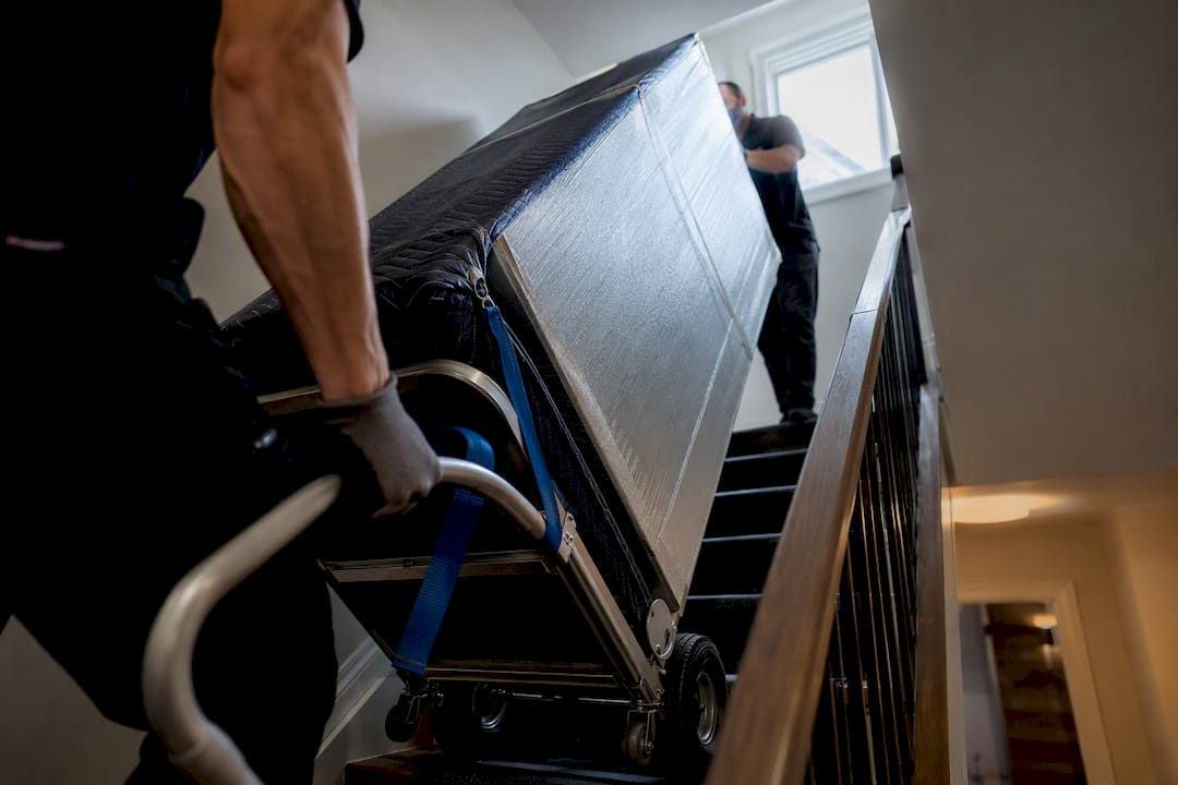 Crew guiding wrapped refrigerator down stairs