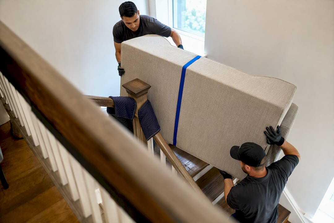 Crew guiding sofa around stair landing