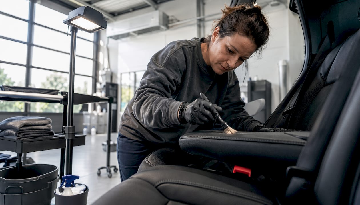Een vrouw maakt haar leren stuur schoon met een zachte borstel.